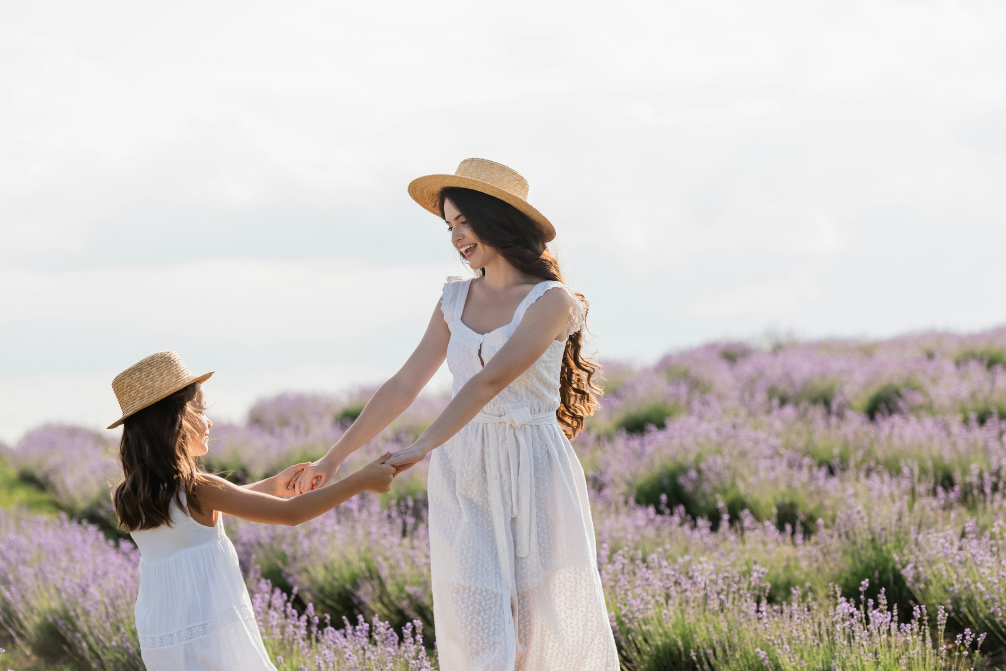joyful mom and daughter in straw hats holding hands while having fun in field