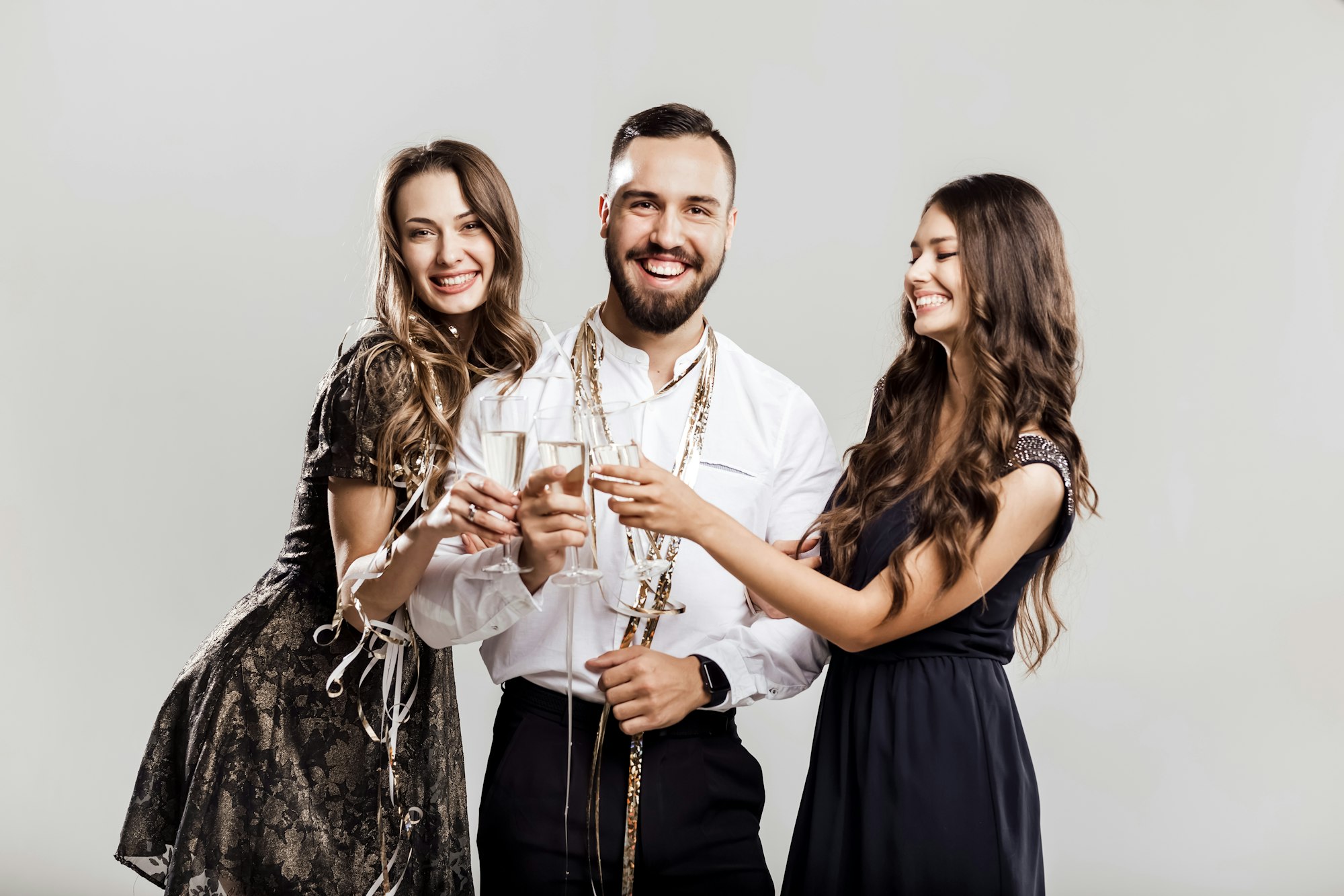 Party time. Two beautiful girls dressed in elegant dresses and handsome man in the white shirt hold